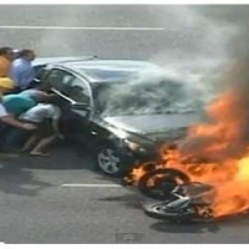 BYSTANDERS LIFT BURNING CAR TO SAVE TRAPPED BIKER